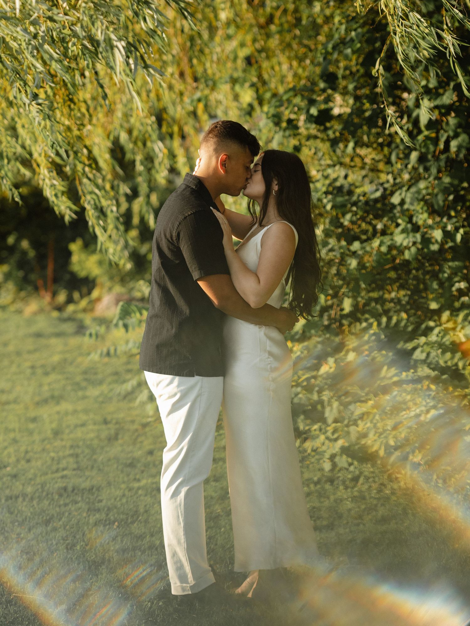 Romantic couple embraces under lush green foliage in an intimate outdoor setting.