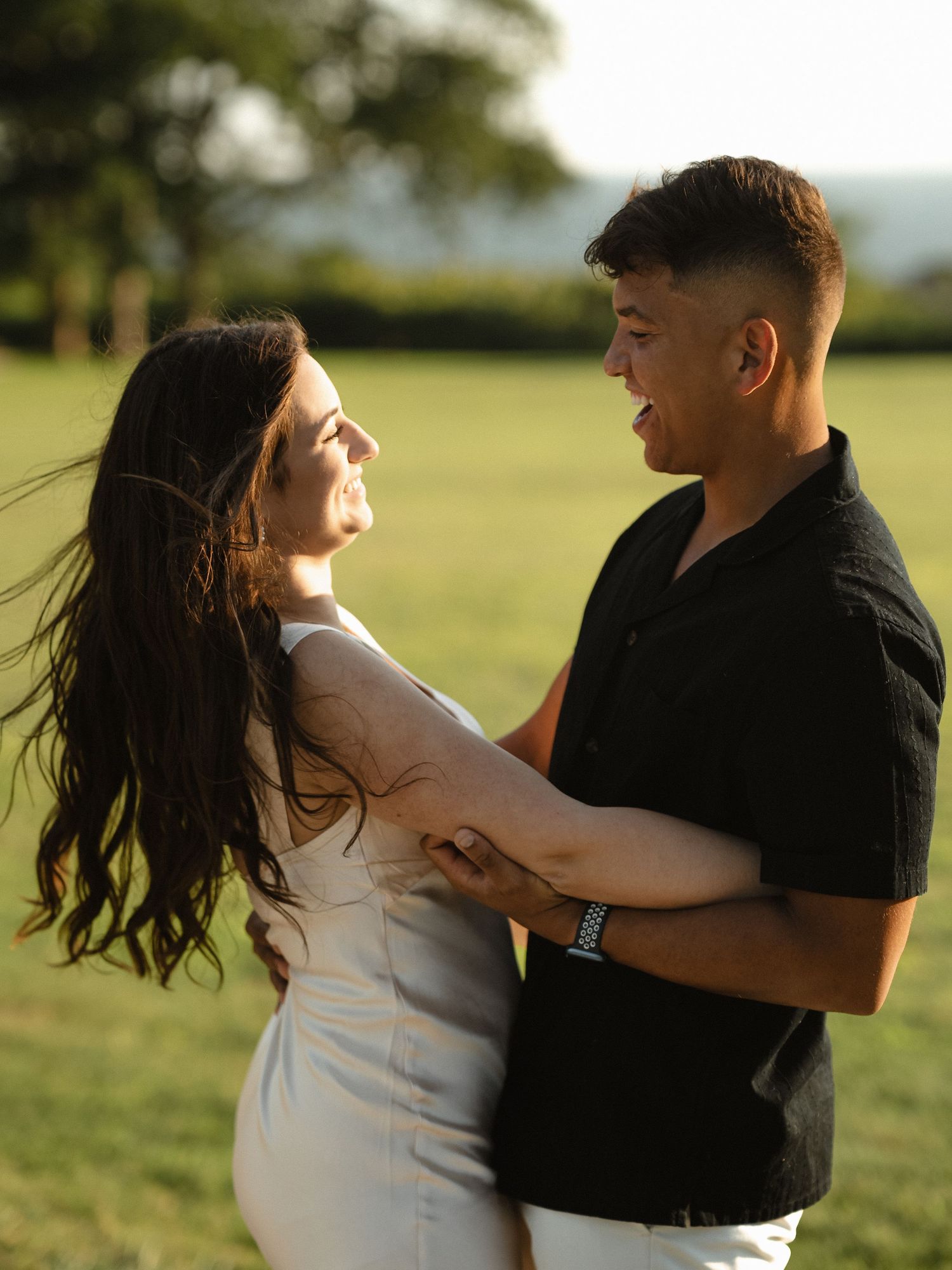 Couple dancing playfully in a sunlit field wearing black and white.