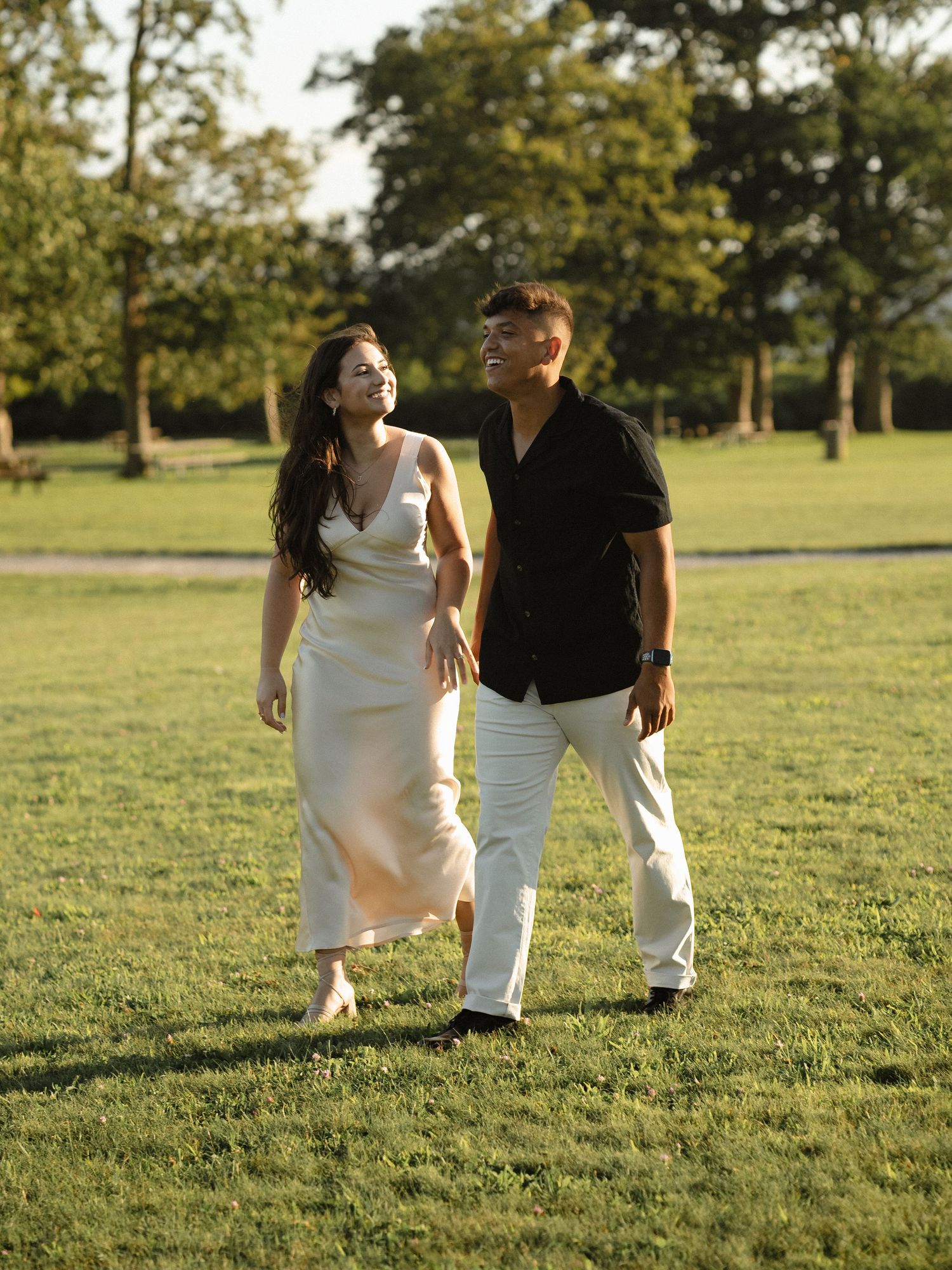 Couple strolling together on grassy field during golden hour.