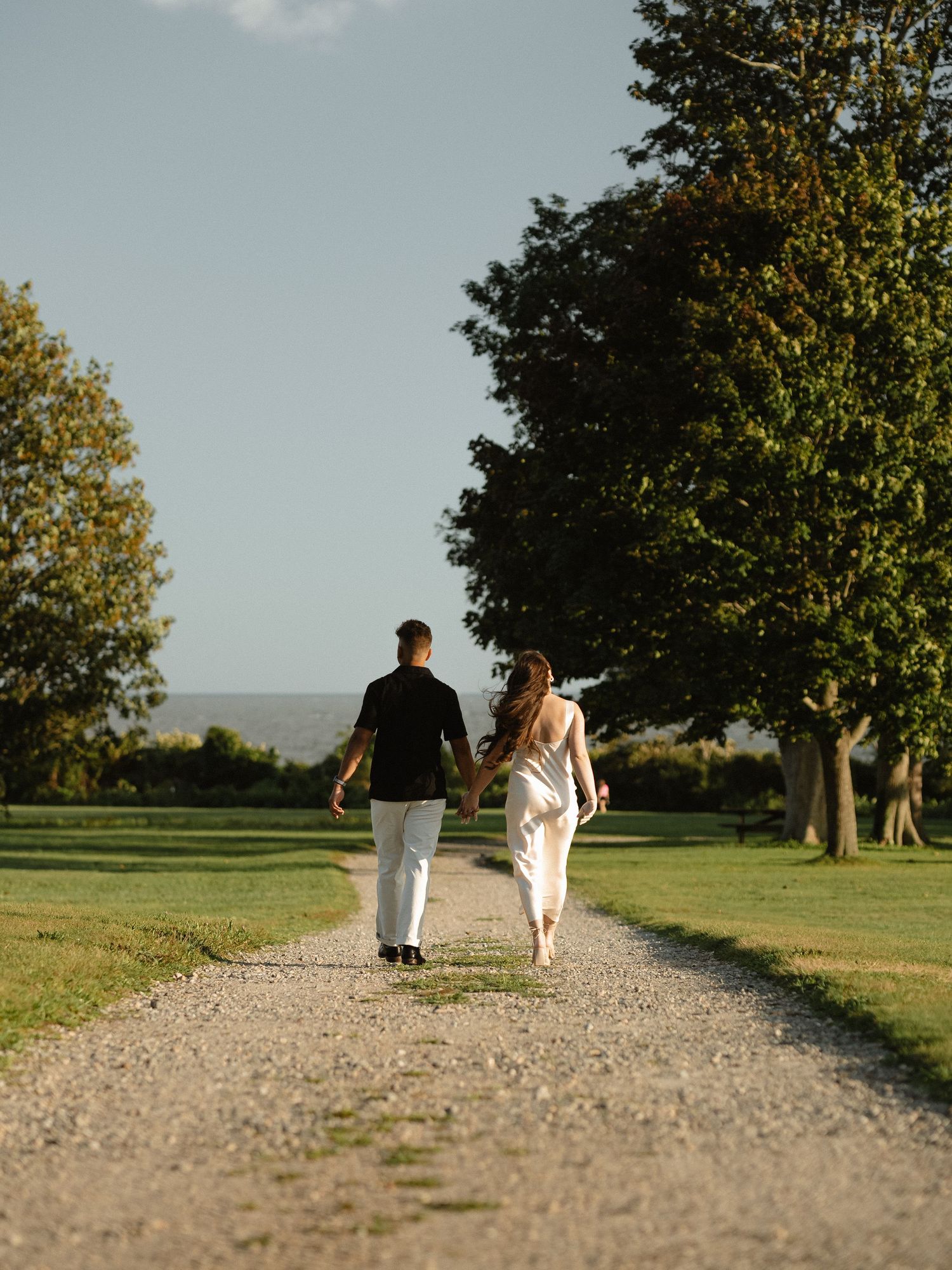 Couple walking away on gravel path through scenic countryside landscape.