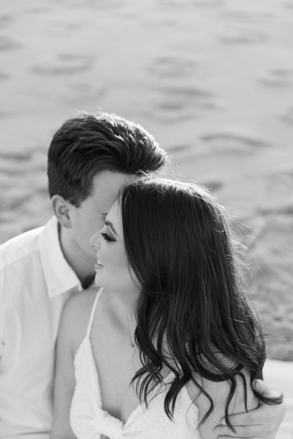 Black and white close-up of a couple sharing a tender romantic moment by the water.