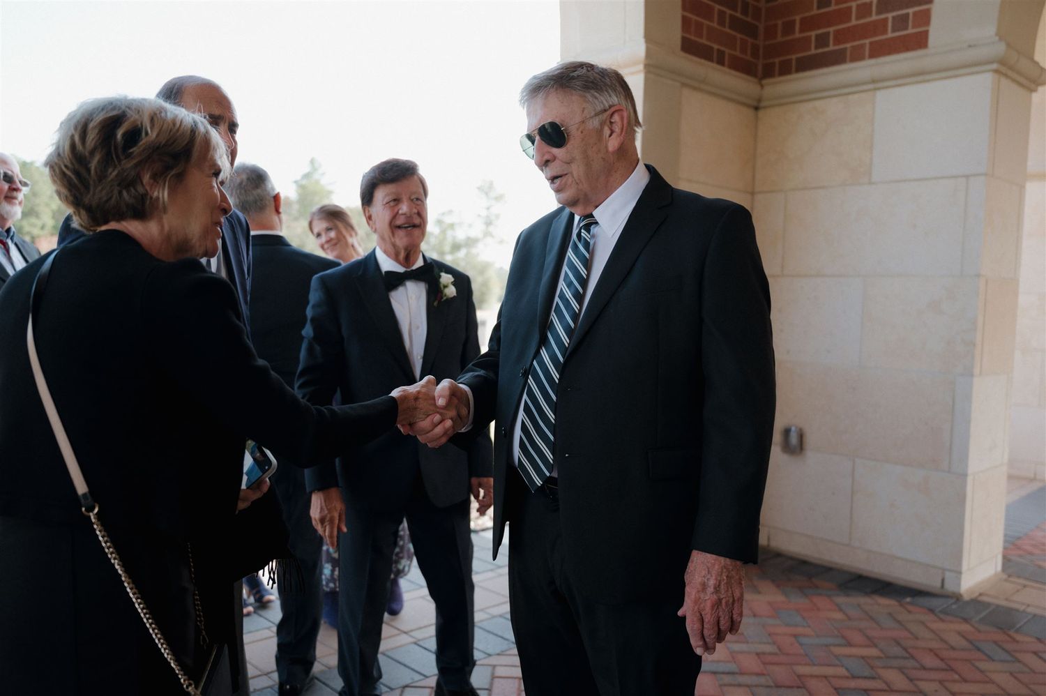 Formal handshake between wedding guests during an outdoor reception.