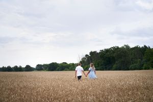 Couple walking hand in hand through golden wheat field at sunset.