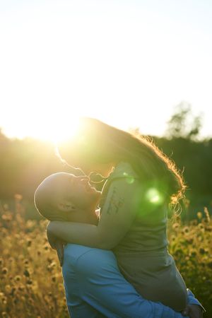 Silhouette of embracing couple backlit by warm sunset in meadow with wildflowers.