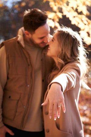 Engaged couple sharing intimate moment in autumn sunlight while showing off ring at the Guelph Arboretum.