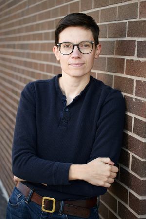 Portrait against brick wall featuring navy sweater and brown leather belt.
