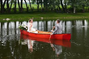 Romantic wedding photo of couple in red canoe on serene lake surrounded by trees and a reflection in the water.