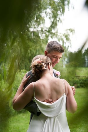 Wedding couple embracing outdoors through willow tree branches.