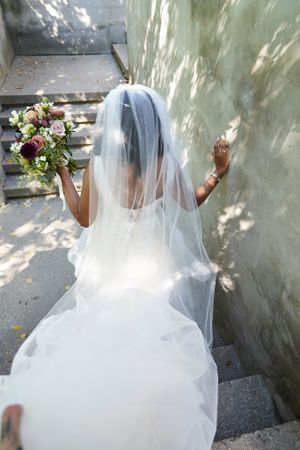 Bride in flowing white dress and veil ascending stone steps with bouquet and speckled light st Langdon Hall.