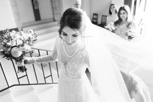 Black and white candid of joyful bride descending staircase in flowing veil at Church of Our Lady.