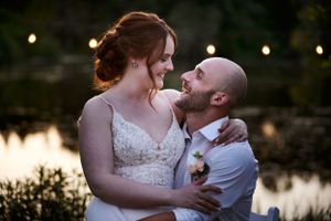 Romantic sunset dusk portrait of newlyweds embracing by a pond with string lights.