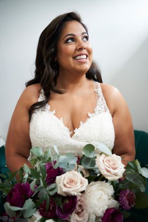 Radiant bride holding elegant bouquet of pink and burgundy flowers looking up to a beam of sunlight.
