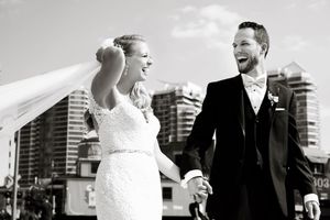 Black and white photo of laughing newlyweds with Toronto city skyline in background.