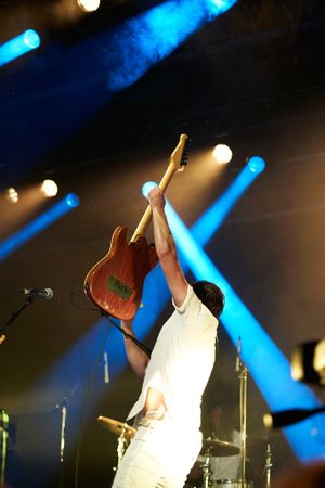 Musician holds electric guitar high above head during performance with blue stage lighting.