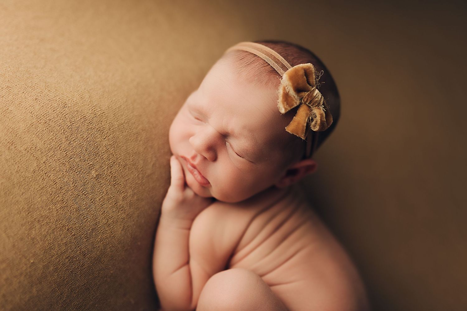 Sleeping newborn with delicate headband in warm-toned professional portrait.