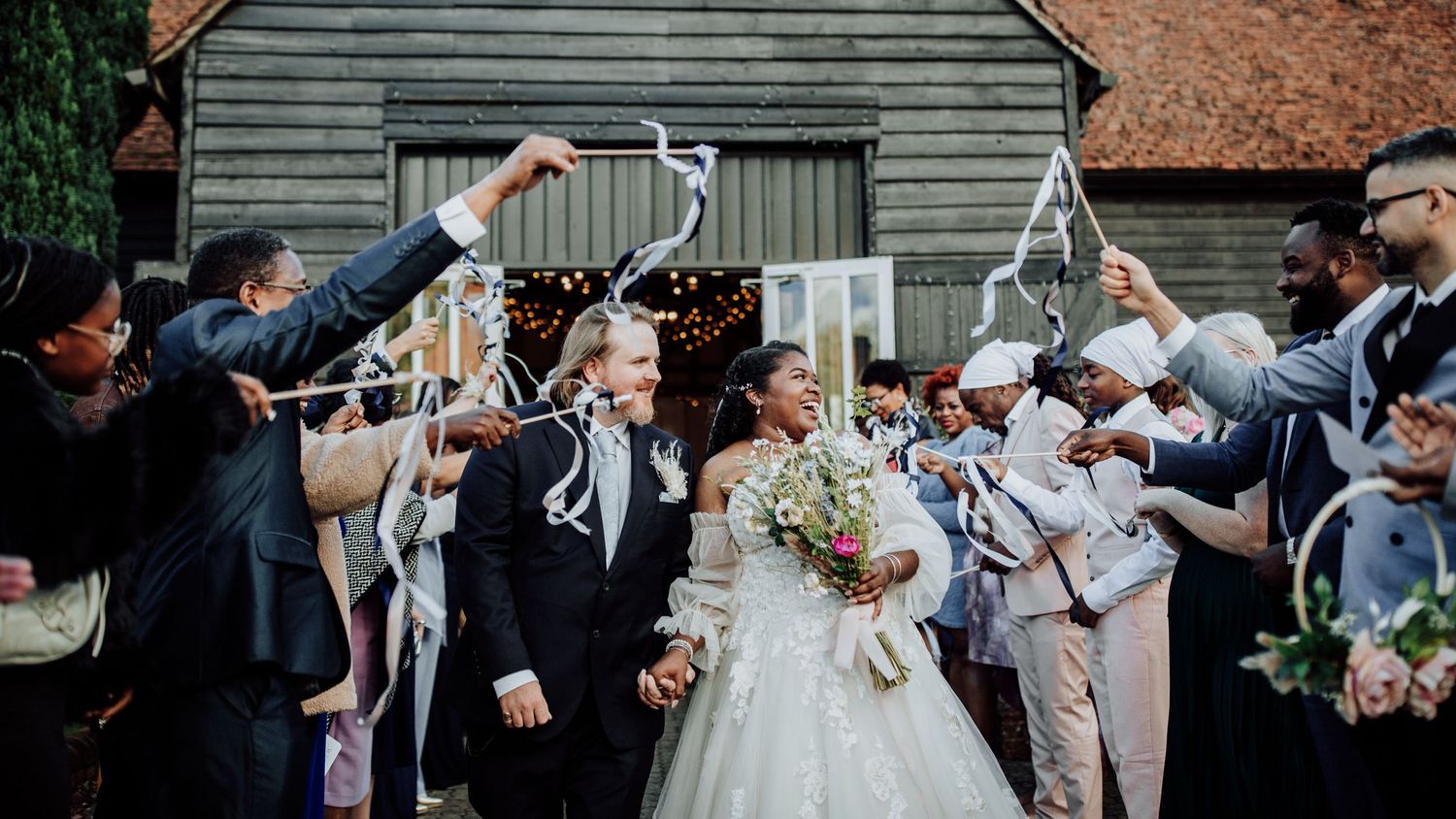 Wedding party celebrates by showering newlyweds with confetti outside a rustic barn.