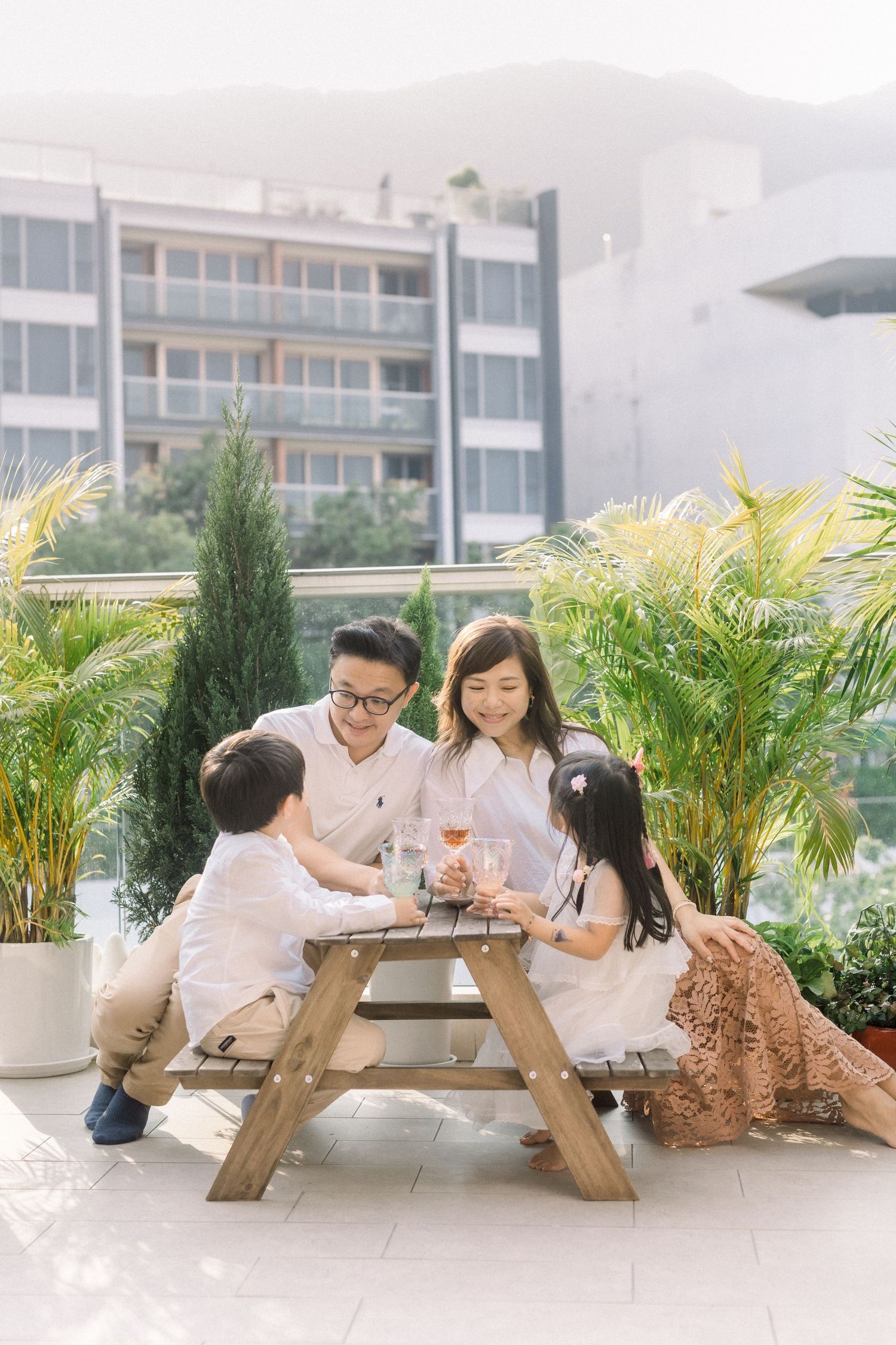 Family gathering around a wooden picnic table on an outdoor terrace with plants.