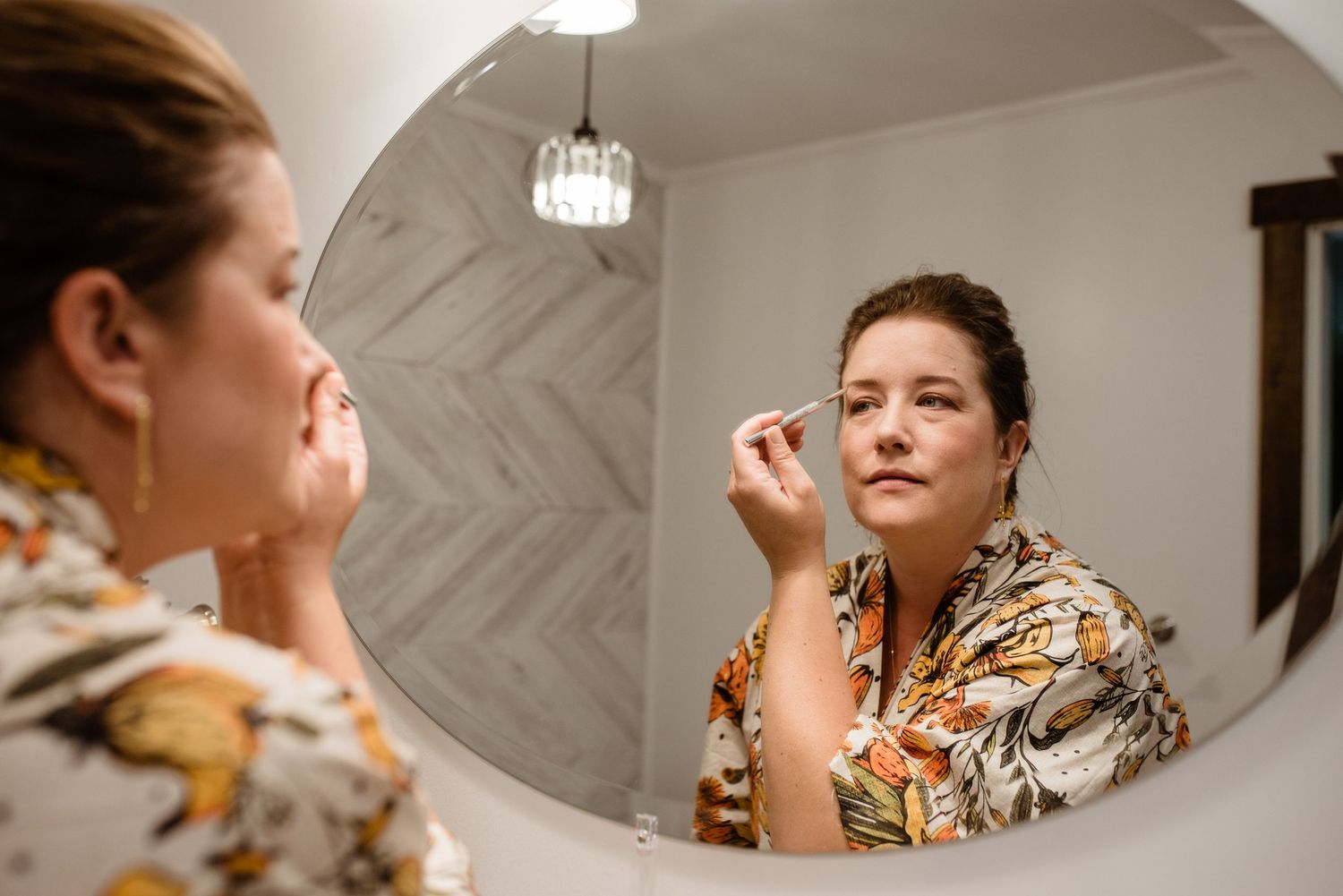 A reflection in a bathroom mirror showing someone applying makeup.