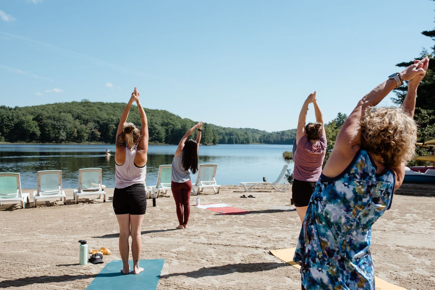 People stretching with raised arms during an outdoor yoga class by a scenic lake.