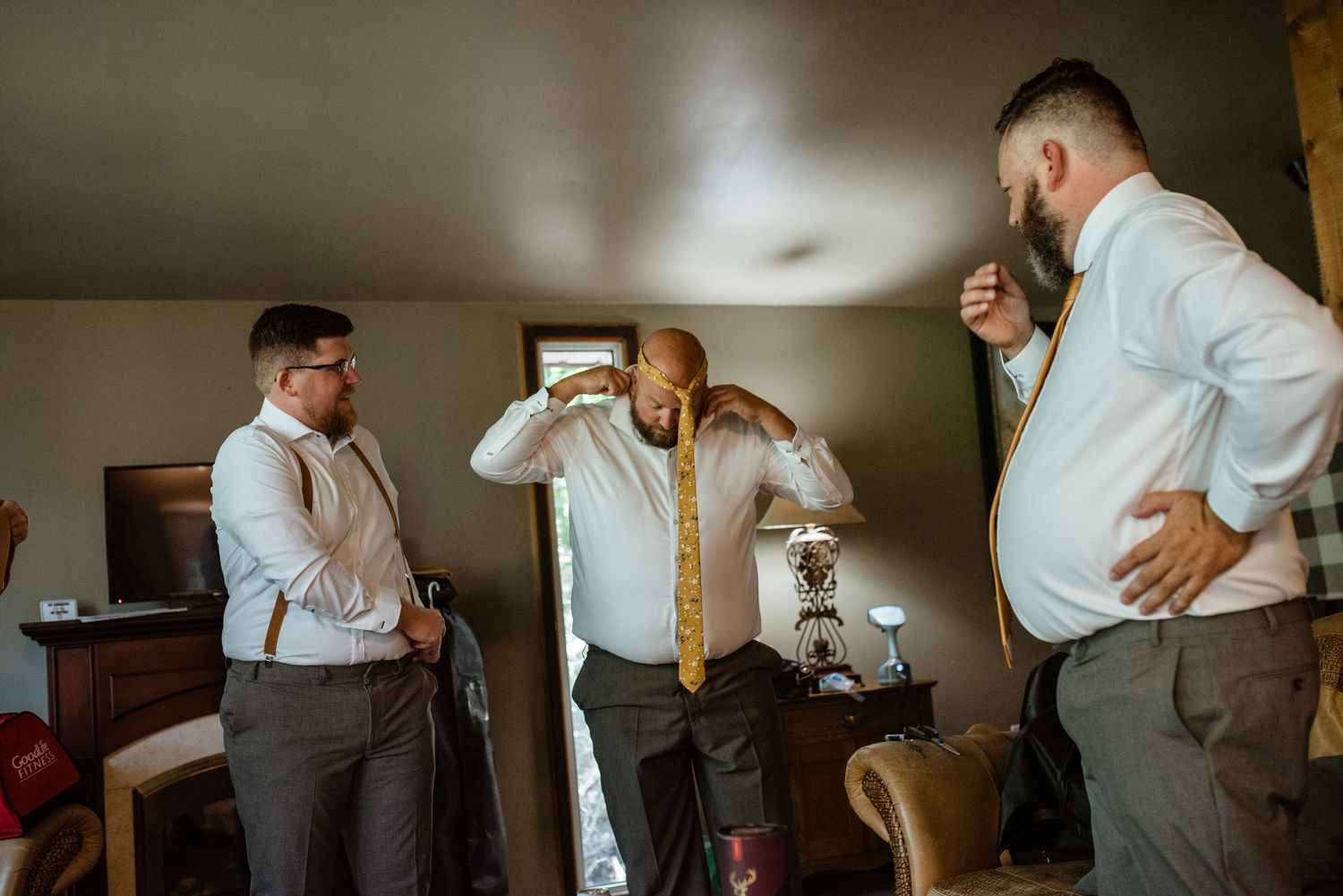 Groomsmen in dress shirts and suspenders laughing together while getting ready for a wedding.