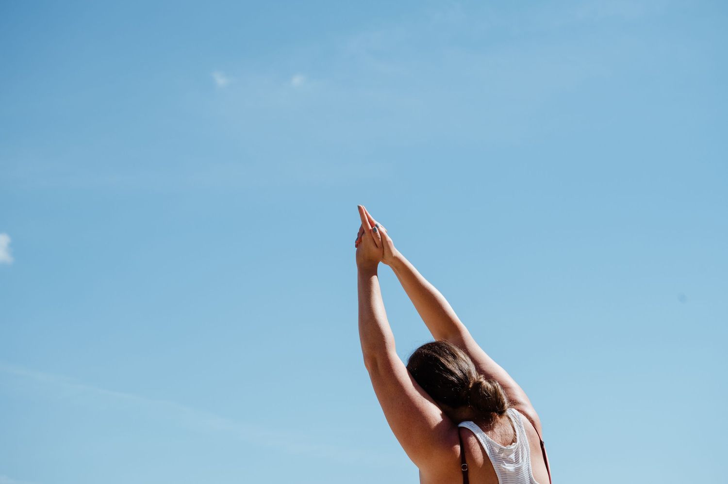 A person stretching arms upward against a bright blue sky during outdoor exercise.