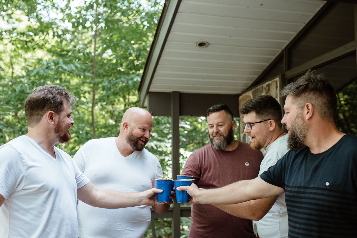 A group of men gathered on a porch looking at something together.