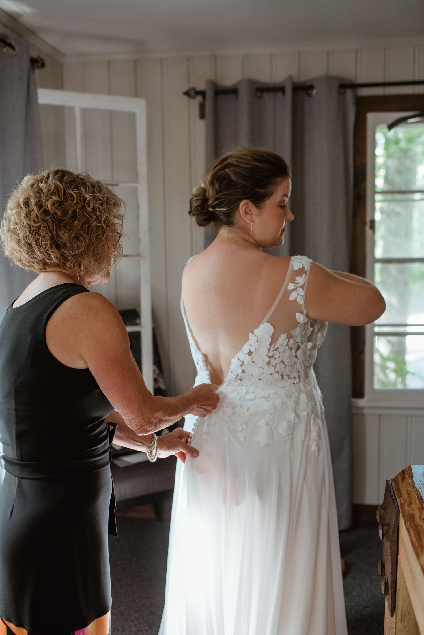 Helper assisting with the fastening of an elegant white lace wedding dress with detailed back.