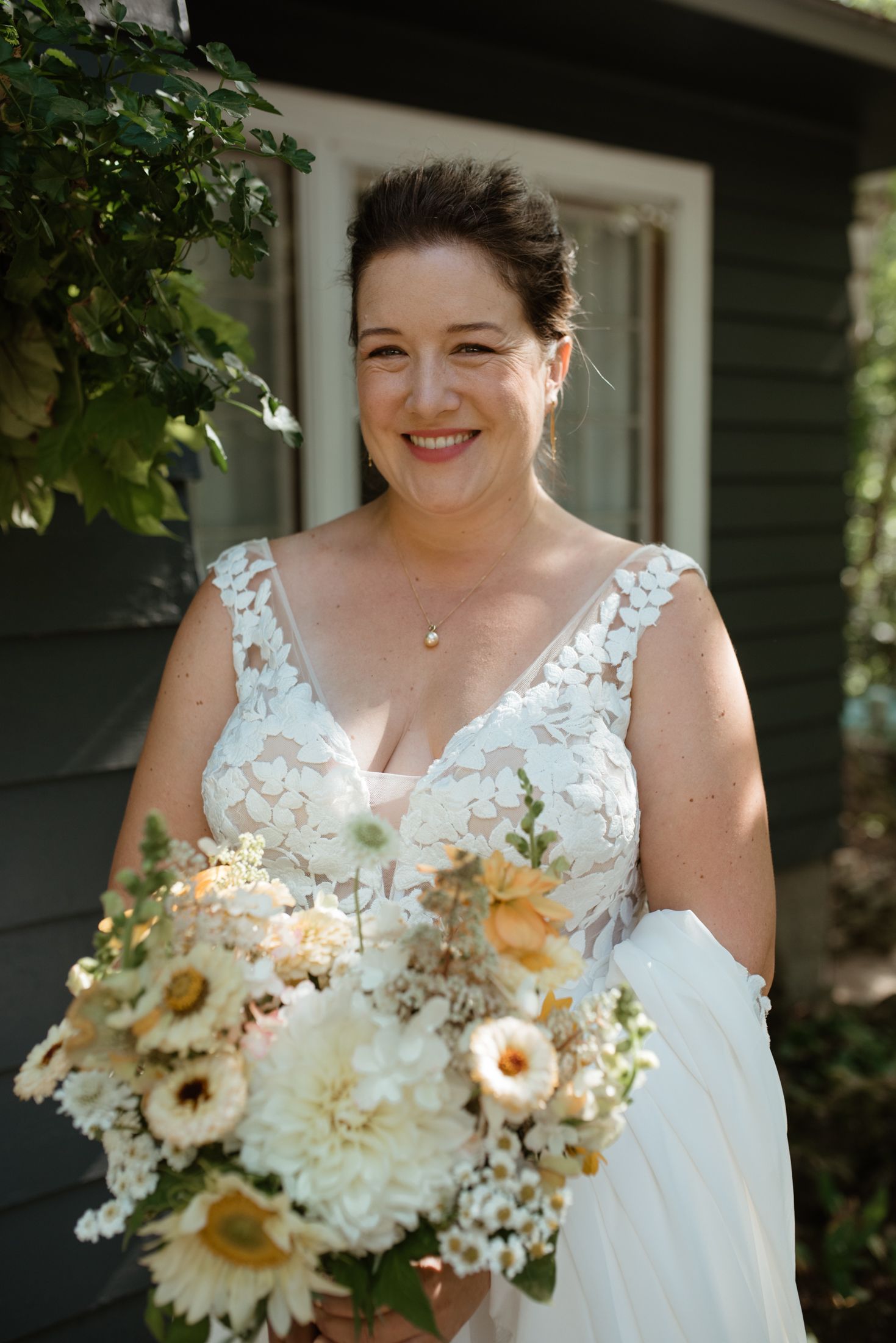 Beautiful wedding portrait with peach and white floral bouquet against dark exterior wall.