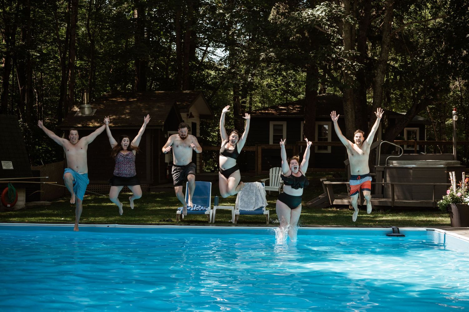 A group of friends jumping into a swimming pool on a summer day.