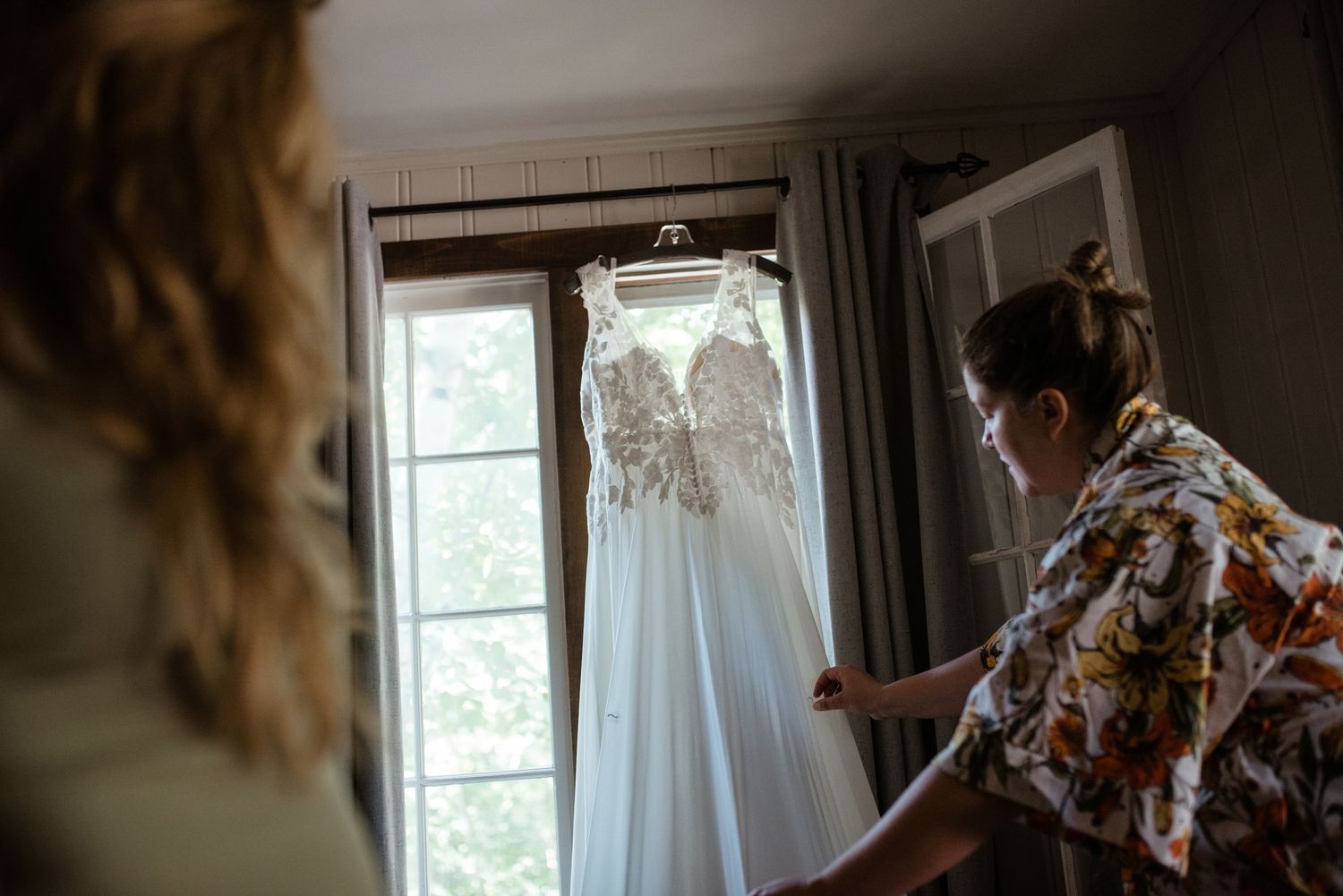 A white wedding dress hanging in front of a window in natural light.