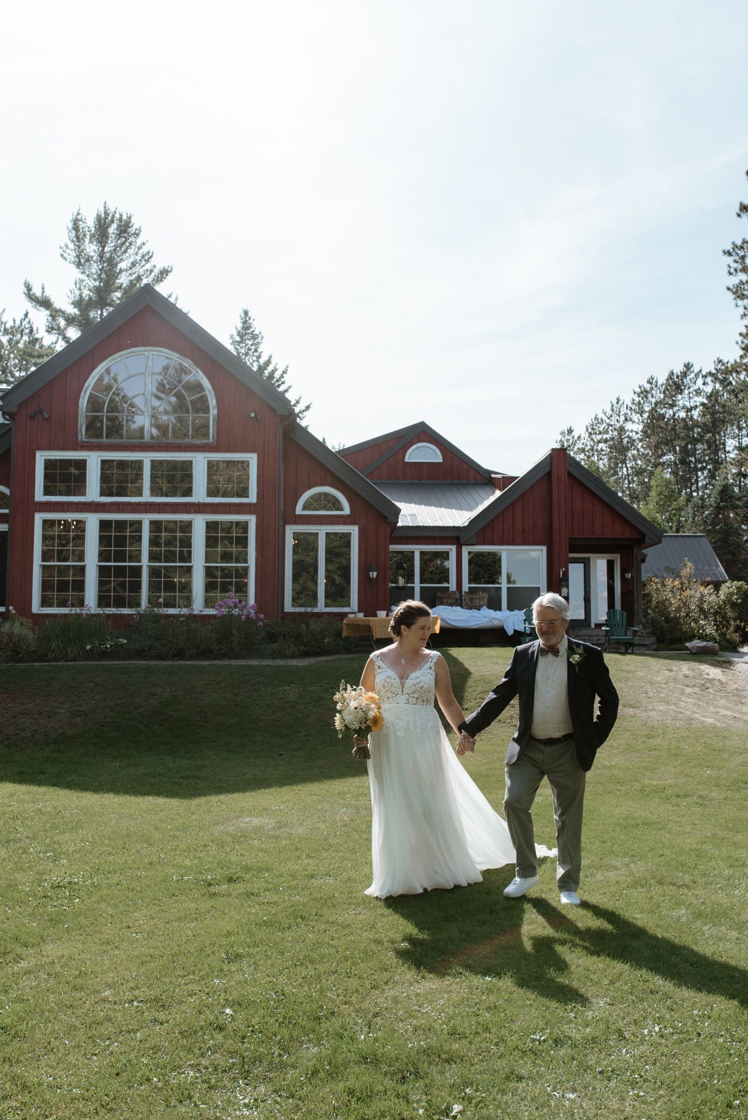 Couple walking on lawn in front of rustic red barn-style building with large windows.