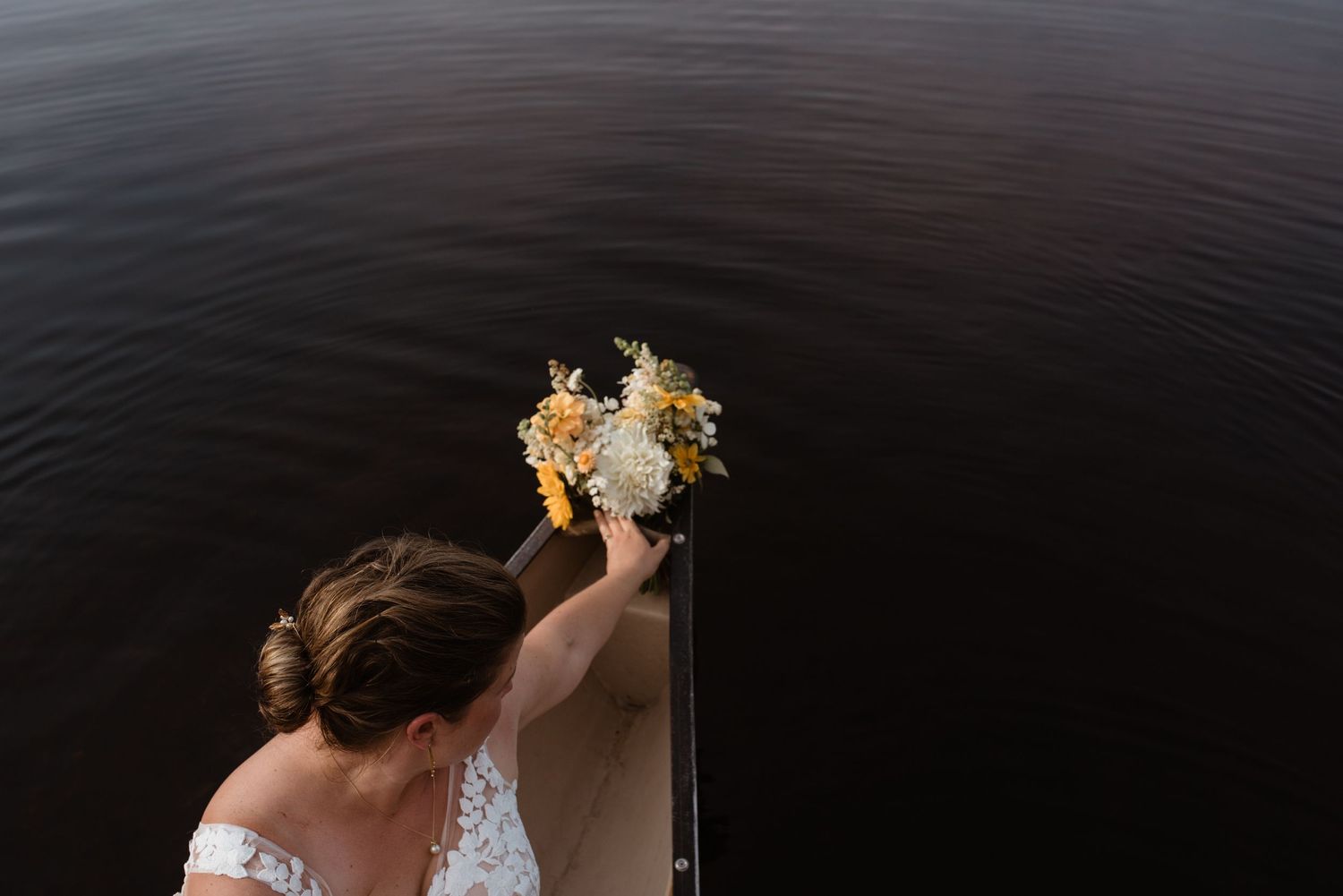 Wedding bouquet held over dark water with white and yellow flowers.