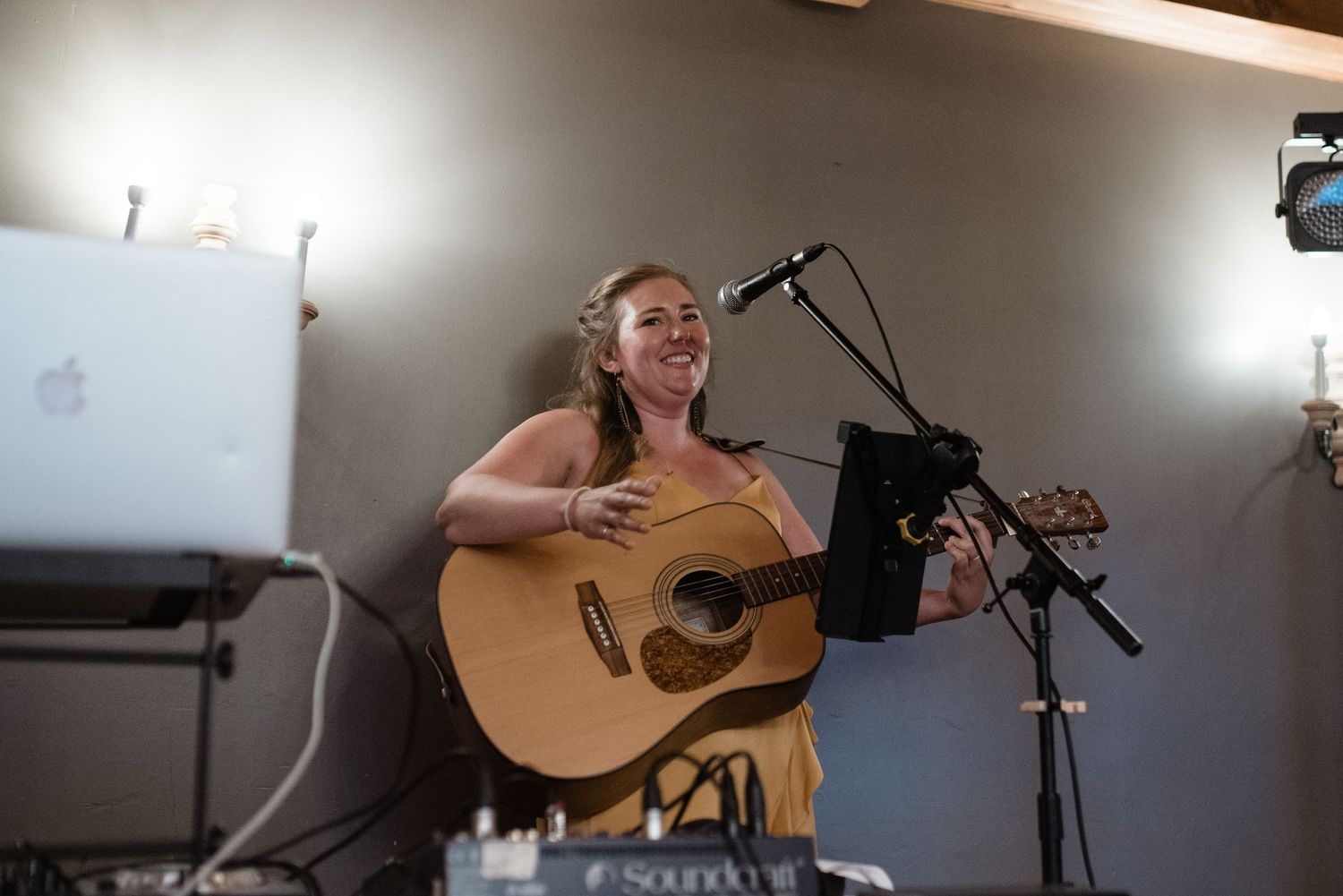Musician performing with an acoustic guitar at an indoor wedding reception.