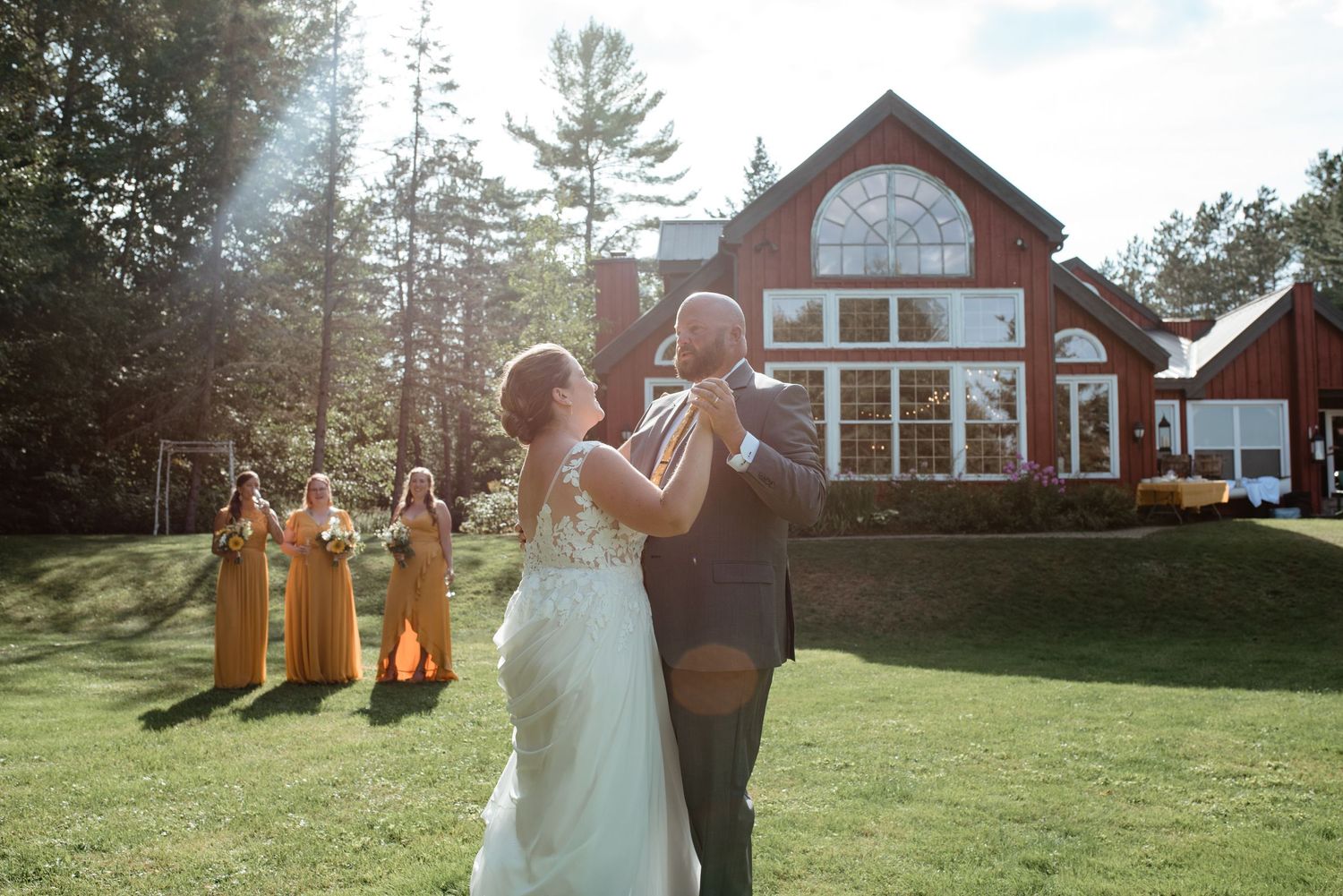 A couple celebrates during their wedding ceremony in front of a rustic red lodge with bridesmaids in yellow dresses.