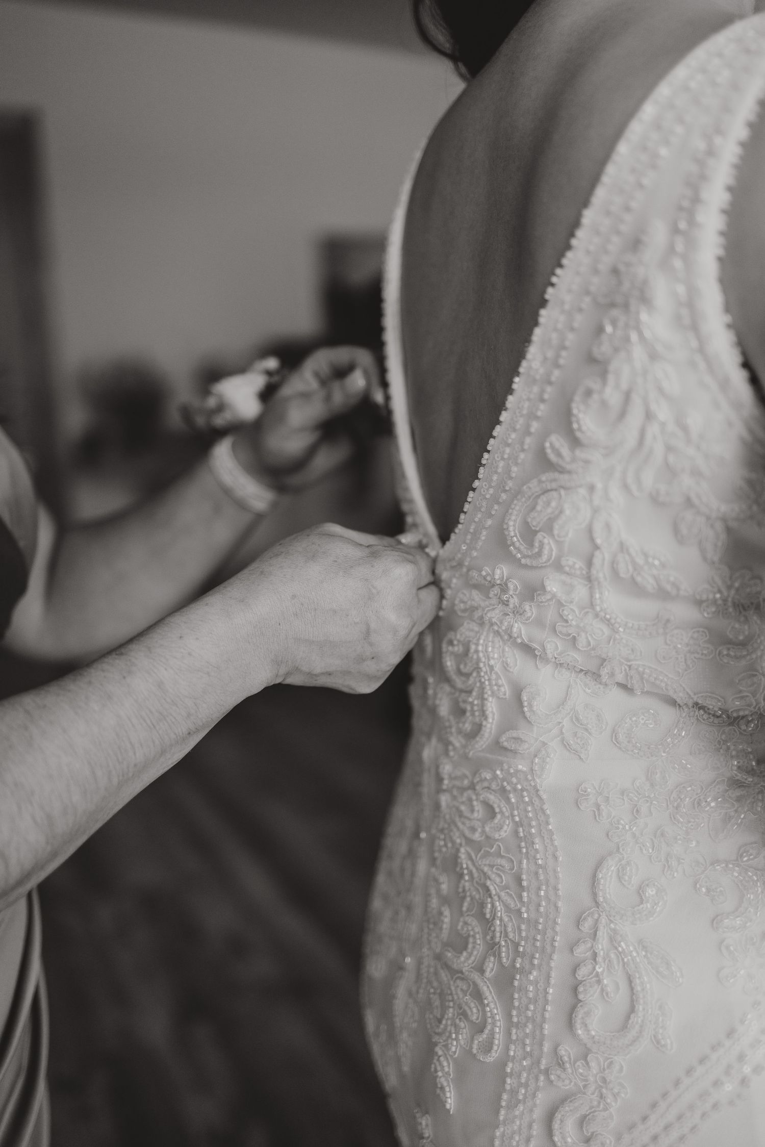 Close-up shot of someone buttoning up an ornate white wedding dress with delicate lace details.