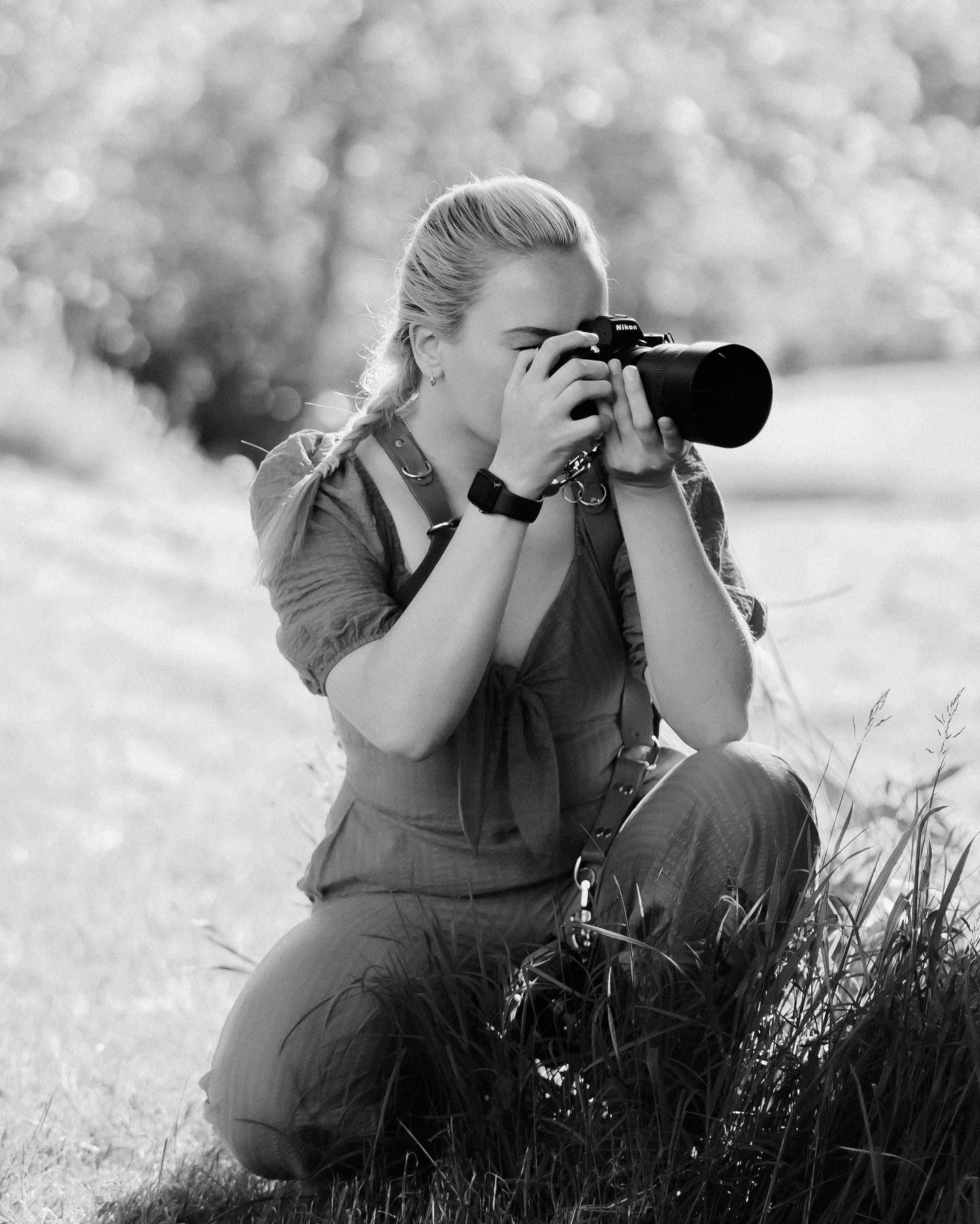 Photographer crouches in grass to take nature photos with professional camera in black and white.