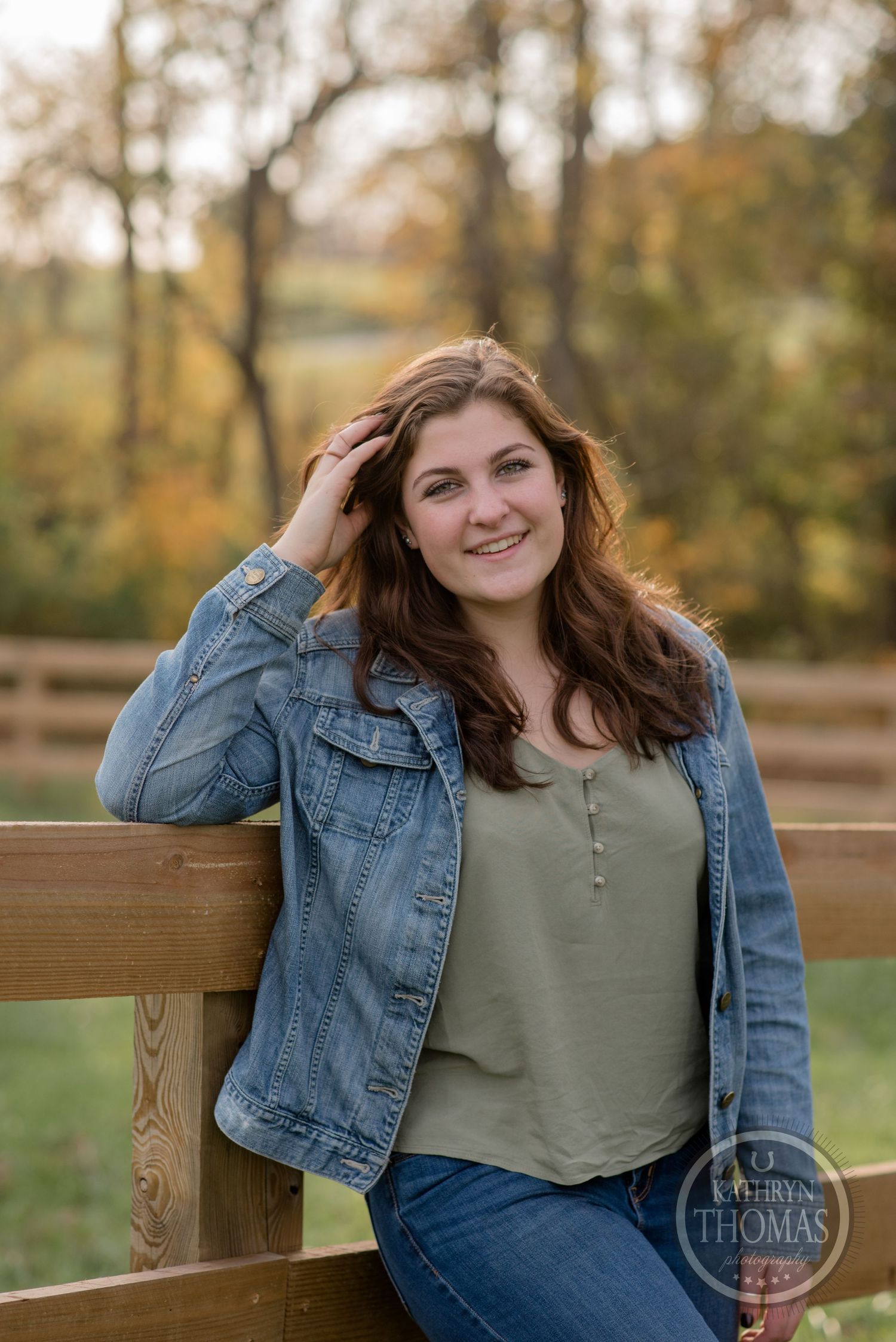 Casual portrait against wooden fence wearing denim jacket and olive top in autumn setting.