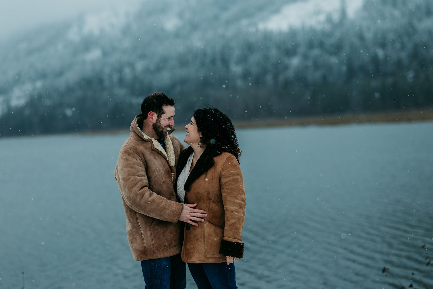 Man and woman gaze lovingly at each other by a wintry lake