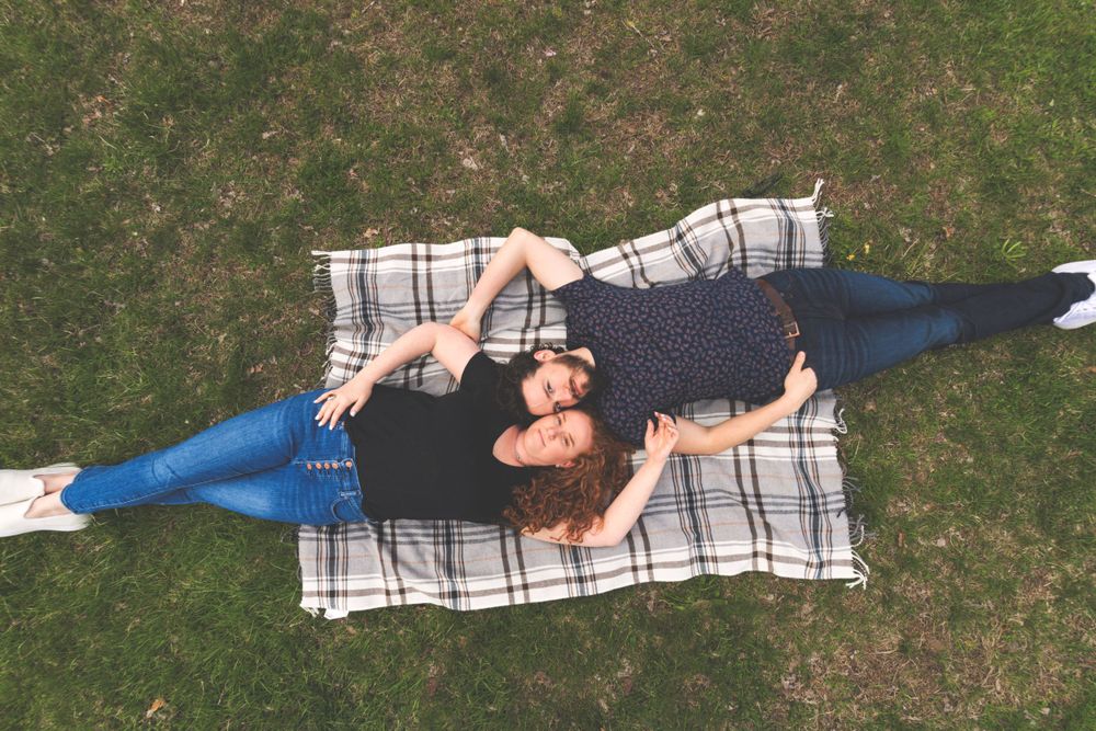 Couple lying together on a checkered blanket on green grass viewed from above.