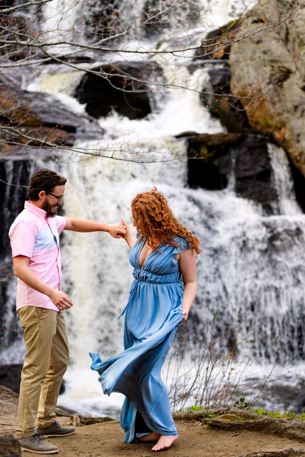 A couple in coordinating outfits dances near a majestic waterfall.