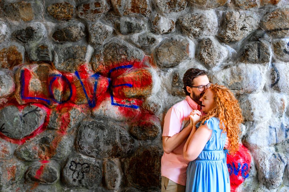 A couple poses against a stone wall with red 'LOVE' graffiti.