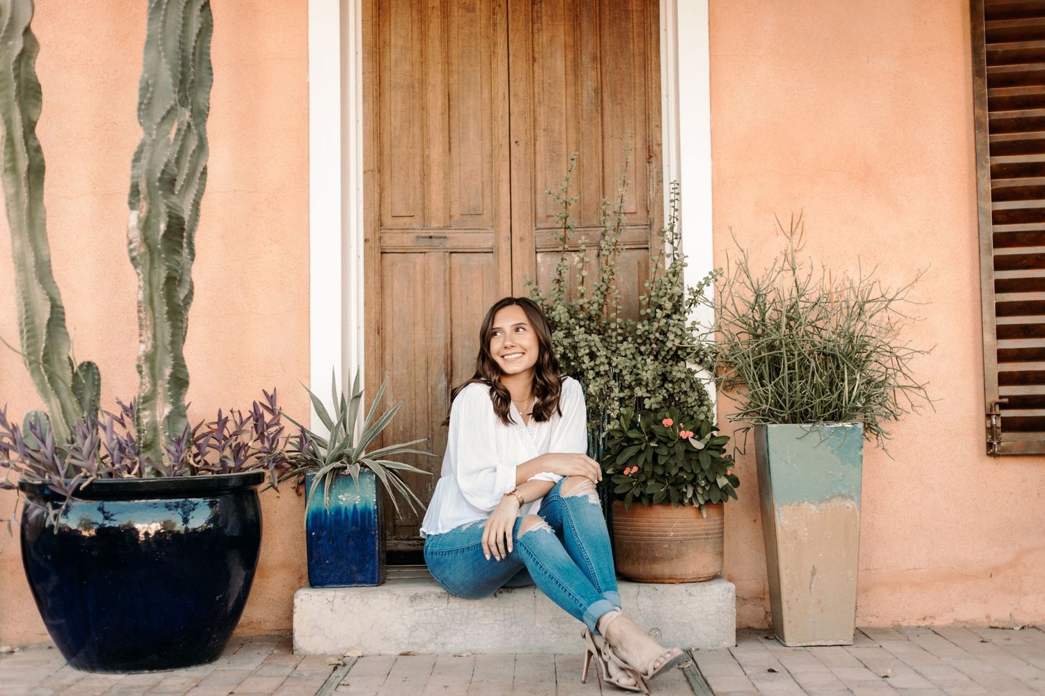 Tucson lifestyle session of a woman sitting on a desert-style porch with cactus plants and warm terracotta walls.