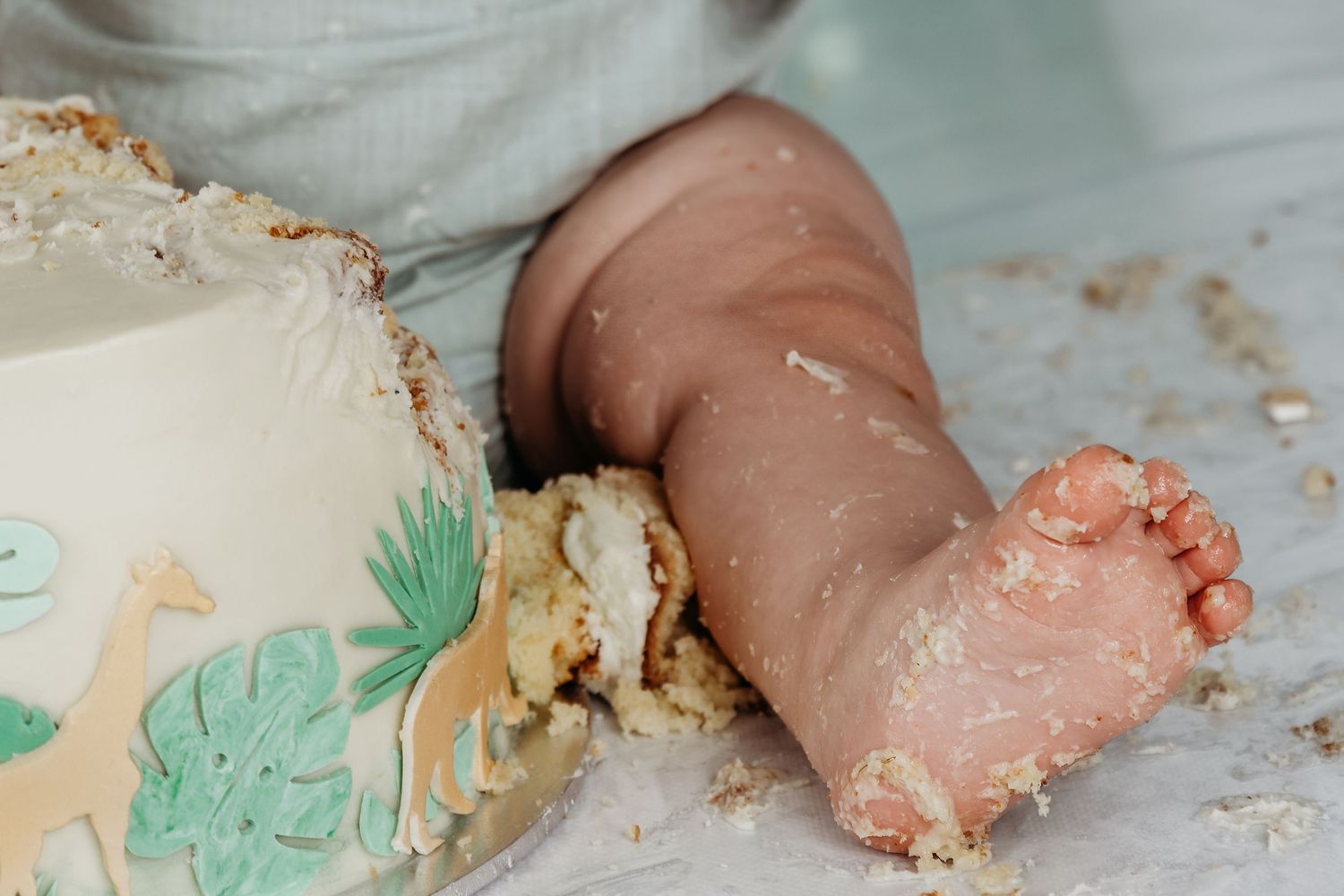 A close-up of a baby's foot covered in white frosting next to a smashed cake.