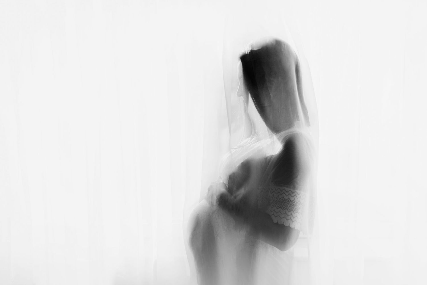 Artistic black and white silhouette of an expectant mother in flowing fabric.