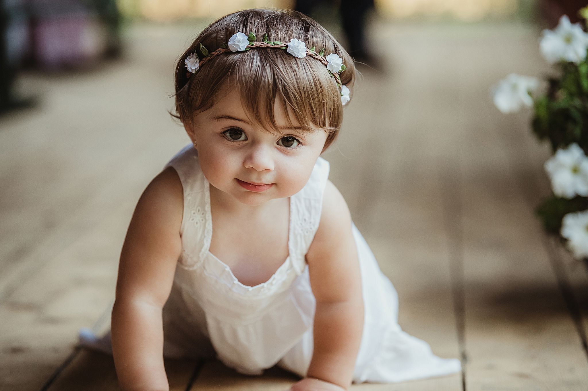 Outdoor portrait of baby wearing floral crown and white dress.