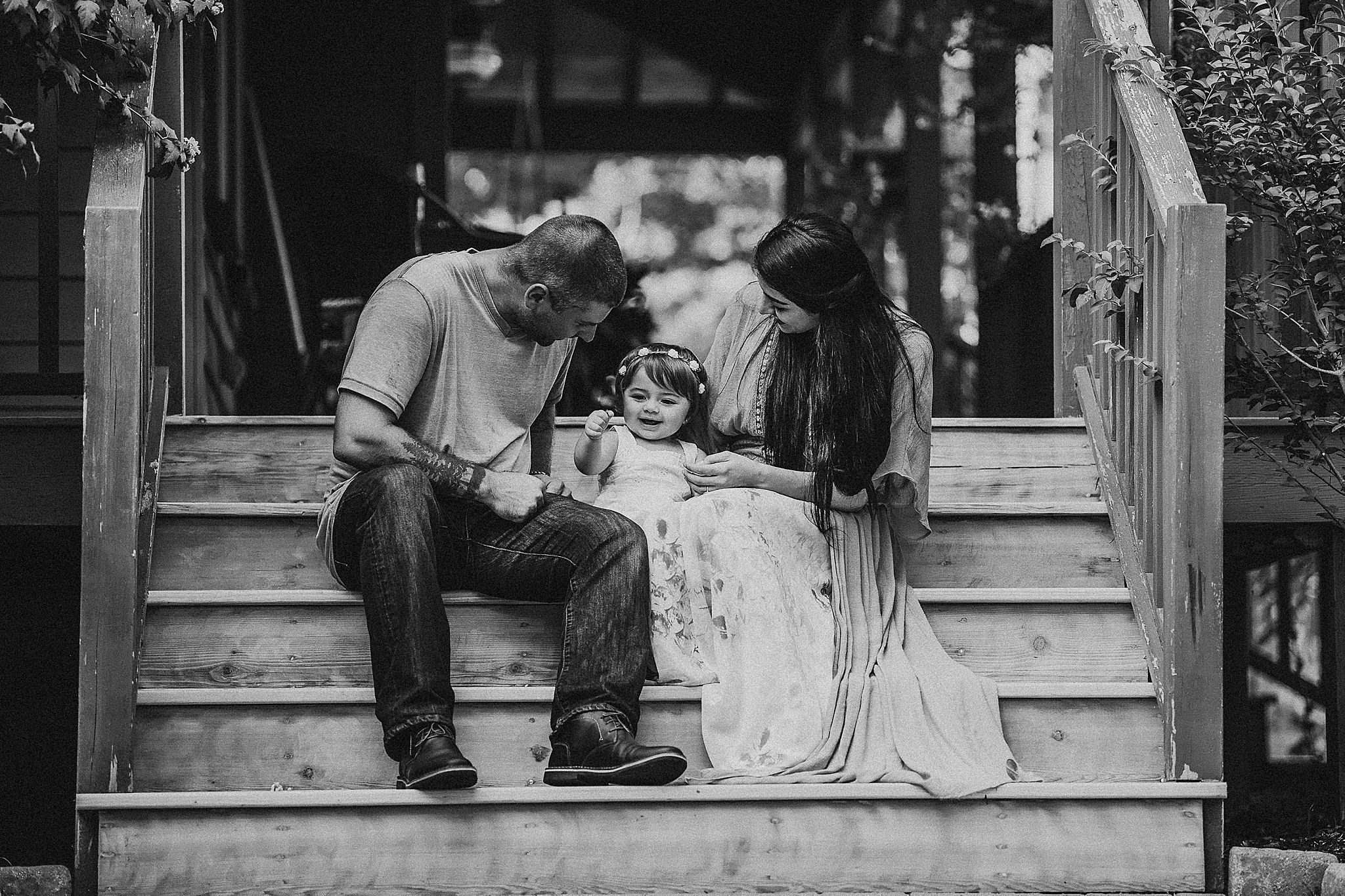 A black and white photo of a family sitting together on wooden porch steps.