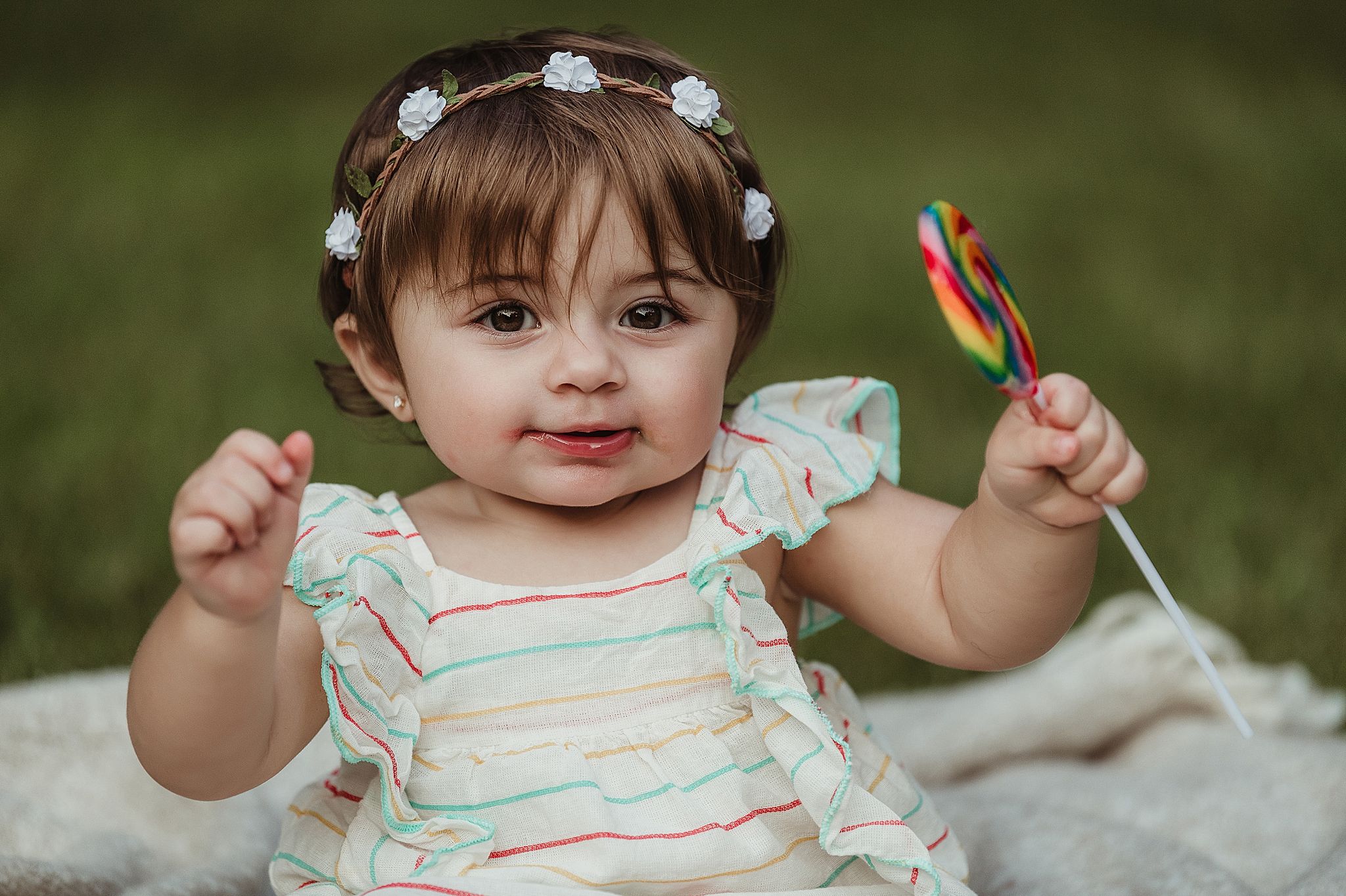 Child in ruffled dress holding up colorful toy against green background.