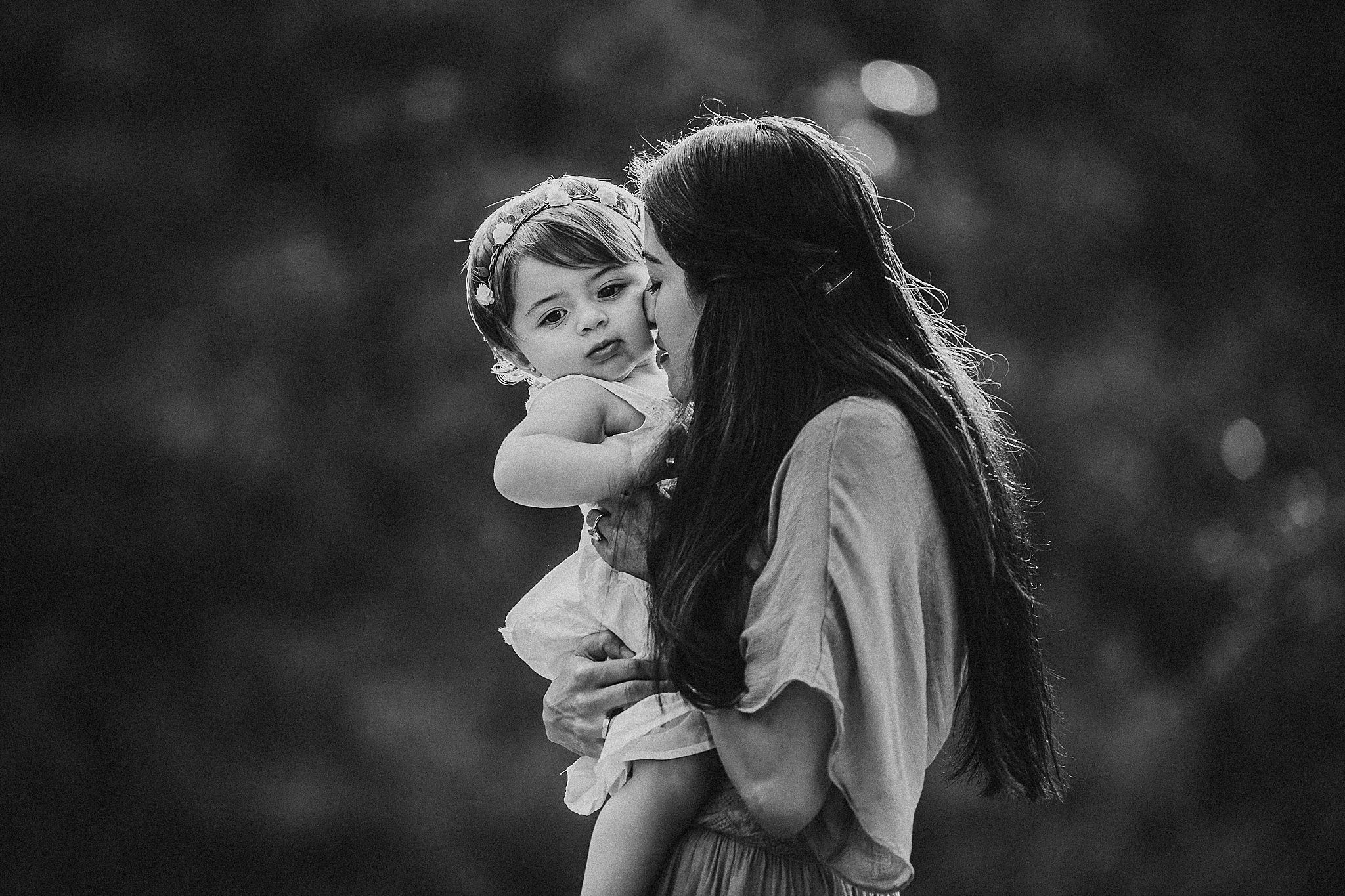 Black and white portrait showing tender moment between parent and child outdoors with bokeh background.
