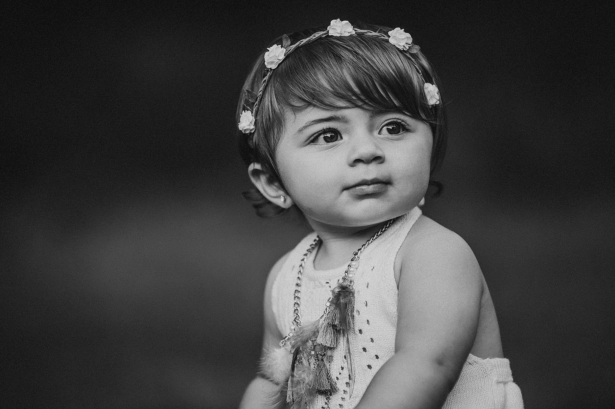 Black and white portrait of toddler wearing floral crown and white dress.