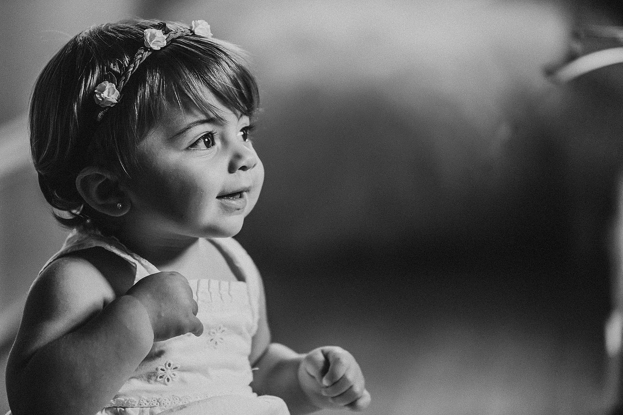 Black and white portrait of small child wearing floral crown and white dress looking to side.